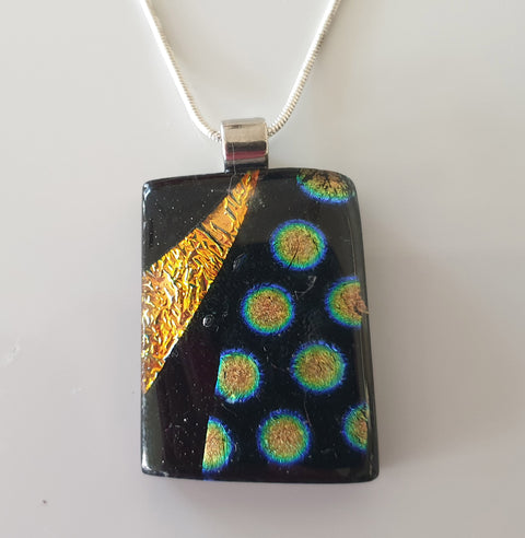 black and gold pendant with bursts of gold and blue dichroic dots